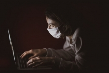 woman in white shirt wearing a mask using laptop computer